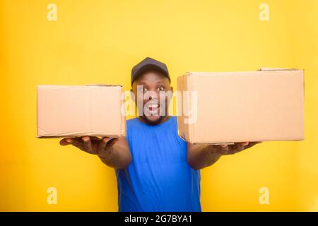 Ein afrikanisches Lieferpersonal oder ein Versandmann, der ein blaues Hemd trägt, Boxen trägt und eine Gesichtskappe trägt Stockfoto