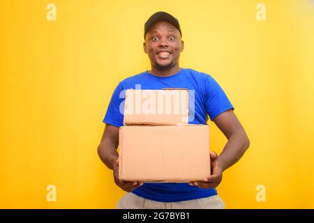 Ein afrikanisches Lieferpersonal oder ein Versandmann, der ein blaues Hemd trägt, Boxen trägt und eine Gesichtskappe trägt Stockfoto