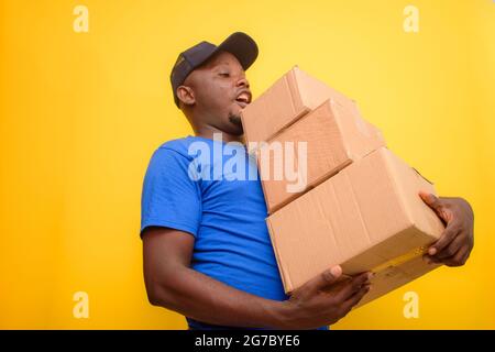 Ein afrikanisches Lieferpersonal oder ein Versandmann, der ein blaues Hemd trägt, Boxen trägt und eine Gesichtskappe trägt Stockfoto