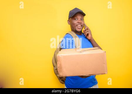 Ein afrikanischer Entsendungsmann mit Rucksack, der einen Anruf abgab, Boxen trug und eine Gesichtskappe trug Stockfoto