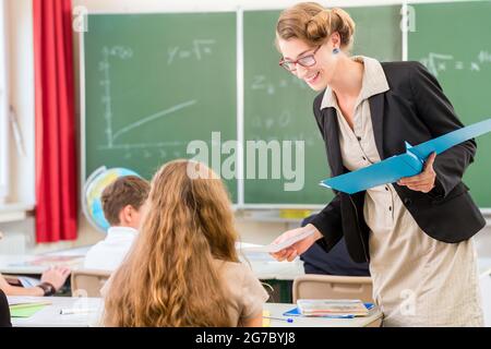 Lehrer oder Dozent oder Pädagoge geben, während die Lektion vor Einer Tafel oder Tafel ein Blatt Papier und Studenten oder Schüler oder Matte Schulen oder unterrichten Stockfoto