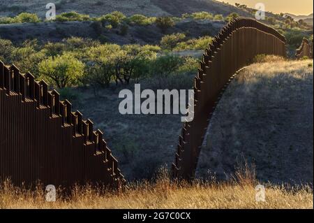 US-Grenzzaun an der mexikanischen Grenze, östlich von Nogales Arizona und Nogales Sonora Mexiko, von der US-Seite aus gesehen, mit Blick nach Südwesten auf den Sonnenuntergang. Stockfoto