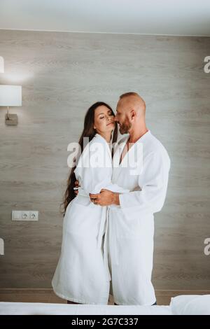 Glückliches Paar in der Liebe, in weißen Roben gekleidet, Kerl umarmt eine Frau auf die Wange küsst. Stockfoto