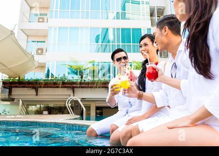 Asiatischen Freunden trinken Cocktails, die von Schwimmbad Stockfoto