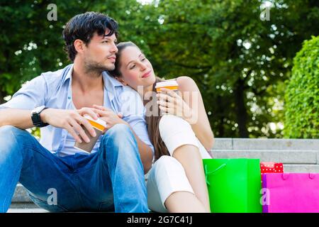 Mann und Frau oder junge Paar Kaffee trinken und sitzen im Stadtpark im Sommer mit Einkaufstüten Stockfoto