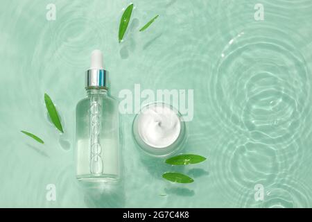 Set von feuchtigkeitsspendenden kosmetischen Produkten auf Wasser mit Tropfen. Glasflasche mit Pipette aus Serum, Kollagen, Glas Creme auf Aqua-Oberfläche mit Wellen-Konzept Stockfoto