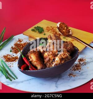 Würzige Hähnchenflügel in schwarzer Schüssel mit Chilischote auf dem Hintergrund in quadratischer Größe Stockfoto