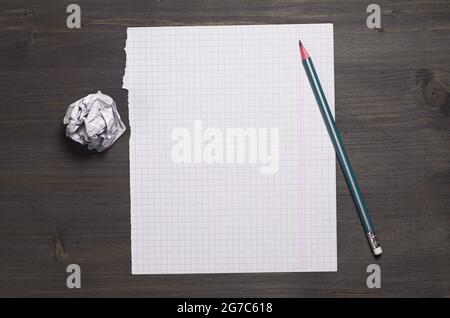 Leeres Blatt aus dem Schulheft, zerknittertes Papier und Bleistift auf dunklem Holzschreibtisch, Draufsicht. Platz für Text Stockfoto