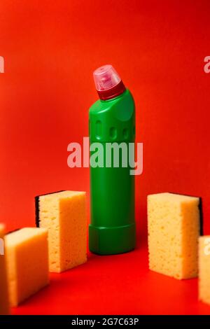 Grüne Flasche mit Reinigungsmittel und Reinigungsschwämmen auf rotem Hintergrund. Stockfoto