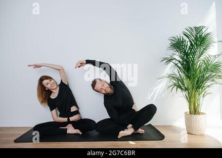 Fröhliches Paar, das sich nebeneinander streckt und auf einer einzigen Matte sitzt Stockfoto