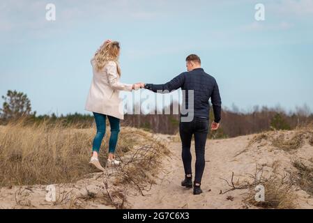 Ein junges Paar, das auf Sanddünen ging, hielt Hände.in der Ferne der Wald.Abenteuer Reise Lifestyle-Konzept. Stockfoto