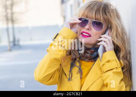 Frau mittleren Alters, die auf der Straße mit Sonnenbrillen auf dem Handy spricht Stockfoto