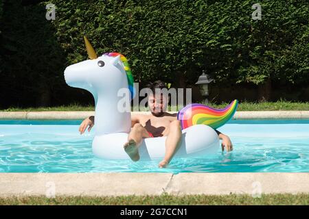 Junger glücklicher Mann auf einem großen aufblasbaren Einhorn-Ring in einem Schwimmbad. Sommerkonzept. Stockfoto