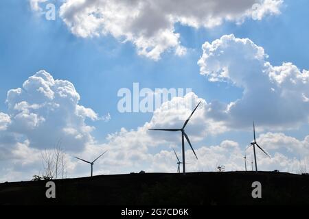 Silhouette von Windturbinen auf einem Hügel mit dem Hintergrund eines blauen Himmels mit vereinzelten Wolken. Stockfoto