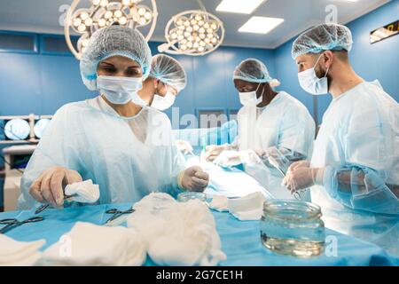 Ein internationales Ärzteteam führt eine komplexe chirurgische Operation an einem unter Anästhesie stehenden Patienten durch. Moderner Operationssaal und erfahrene Chirurgen Stockfoto