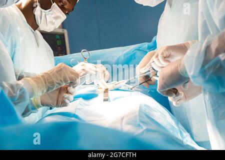 Ein internationales Ärzteteam führt eine komplexe chirurgische Operation an einem unter Anästhesie stehenden Patienten durch. Moderner Operationssaal und erfahrene Chirurgen Stockfoto