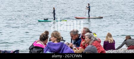 Urlauber auf Stand Up Paddleboards paddeln an einem kalten Tag in Cornwall am Strand von Polgwidden Cove am Helford River vorbei. Stockfoto