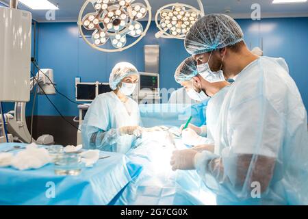 Ein internationales Ärzteteam führt eine komplexe chirurgische Operation an einem unter Anästhesie stehenden Patienten durch. Moderner Operationssaal und erfahrene Chirurgen Stockfoto