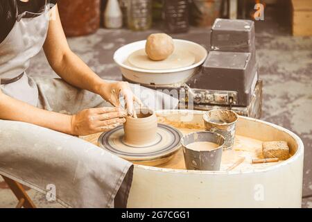 Die Nahansicht eines Töpfers aus weiblichem Töpfchen ergibt aus einer ziegelartigen großen flachen Platte aus Ton auf einem Holztisch in einer Werkstatt. Mit dem Töpfer aus weiblichem Ton Stockfoto
