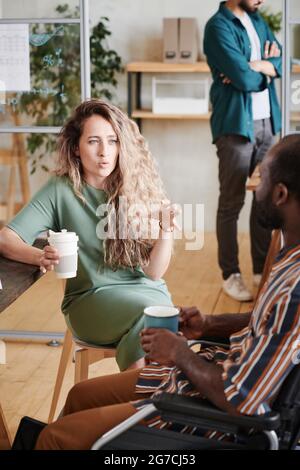 Junge Geschäftsfrau im Gespräch mit ihrem Kollegen, während sie gemeinsam im Büro Kaffee trinken Stockfoto