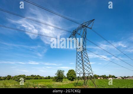 Hochspannungsturm, Stromleitung mit elektrischen Kabeln und Isolatoren auf dem Land vor einem blauen Himmel mit Wolken. Padan-Ebene oder Po-Tal, Italien. Stockfoto