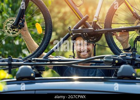 Lächelnder Radfahrer, der sein Fahrrad auf der Dachgepäckträger des Autos montiert Stockfoto