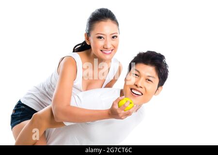 Asiatische junge Mann trägt Frau Huckepack, Obst zu essen und Spaß haben Stockfoto