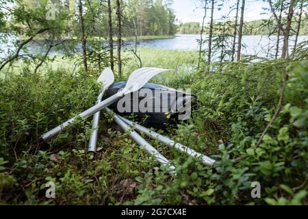 Neues Schlauchboot und Ruder liegen im Gras, am Ufer des Sees. Vorbereitung auf eine Bootsfahrt oder Angeln. Aktiver Lebensstil. Stockfoto