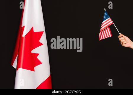 Beschnittene Ansicht des Mannes, der die amerikanische Flagge in der Nähe des kanadischen Symbols auf Schwarz hält Stockfoto