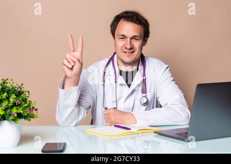 Jungen gutaussehenden Arzt Mann mit Stethoskop über isoliert weißer Hintergrund lächelnd mit glücklichen Gesicht in die Kamera winking tun Sieg unterzeichnen. Anzahl Stockfoto