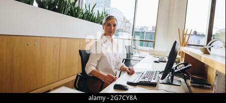 An der Rezeption im Büro sitzt eine ältere Dame an der Rezeption. Ältere Frau, die an der Rezeption des Büros arbeitet. Stockfoto