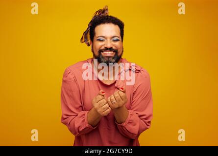 Glücklicher bärtiger Mann in weiblichem Outfit und Make-up. Ziehen Sie Queen Gefühl aufgeregt auf gelbem Hintergrund. Stockfoto
