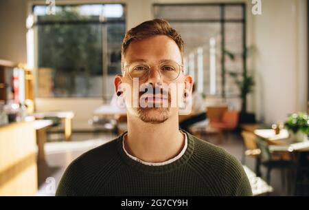 Männlicher Unternehmer, der in kooperierenden Büroflächen steht. Geschäftsmann mit Brille und Blick in die Kamera. Stockfoto