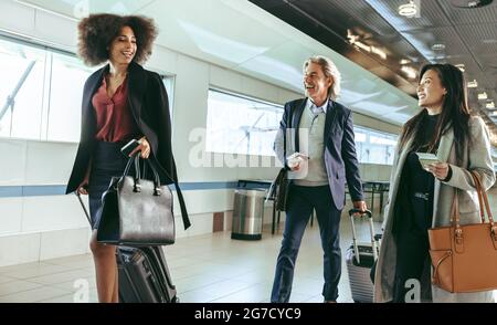 Passagiere, die mit Gepäck auf dem Korridor des Flughafens unterwegs sind. Lächelnde Geschäftsleute, die auf Geschäftsreise sind, tragen Koffer, während sie durch den flughafen laufen Stockfoto