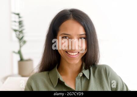 Nahaufnahme des Porträts einer ruhigen, schönen indischen dunkelhaarigen Frau. Die hübsche Mixed-Race-Dame in legerer Kleidung blickt mit einem charmanten, toothy Lächeln auf die Kamera Stockfoto