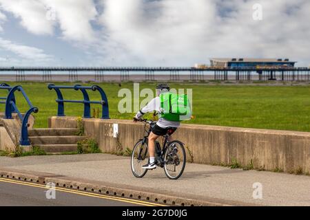 Southport, Merseyside. Wetter In Großbritannien. 13. Juli 2021: Uber-Essen liefern sich bei frühem Sonnenschein und Temperaturen von bis zu 20 Grad Celsius, während die Anwohner an der Strandpromenade des Resorts leichte Übungen machen. Aktivitäten auf der Küstenstraße als Lebensraum für Dünen und die Vergrabung des Sandes (Akkretion) scheinen sich bis zur Fylde-Küste auszudehnen. Die Sefton-Küste kämpft darum, zwei Eindringlinge abzuwehren – das Meer und zähe Gräser, die über dem Strand sprießen und schließlich den Pier umringen, wenn sich Sanddünen bilden. Kredit; MediaWorldImages/AlamyLiveNews Stockfoto