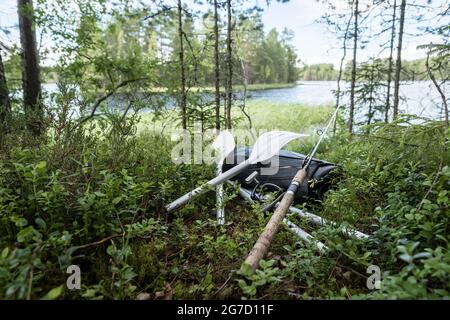 Neu aufgerolltes Schlauchboot, Ruder und eine Spinnrute liegen im Gras, am Ufer des Sees. Vorbereitung für den Fischfang. Stockfoto