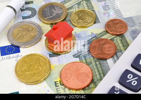 Ein Spielzeughaus auf Euro-Münzen und -Scheinen mit Taschenrechner und Stift. Ein Eigenschaftsfinanzierung Stillleben, Stockfoto