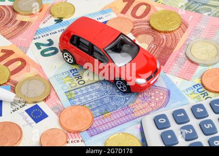 Ein rotes Auto auf Euro-Geldscheinen und -Münzen, das die Fahrzeugfinanzierung darstellt. Stockfoto