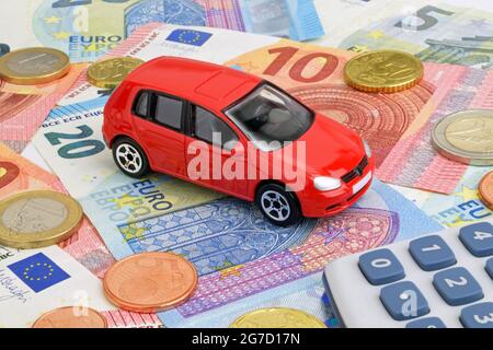 Ein rotes Auto auf Euro-Geldscheinen und -Münzen, das die Fahrzeugfinanzierung darstellt. Stockfoto