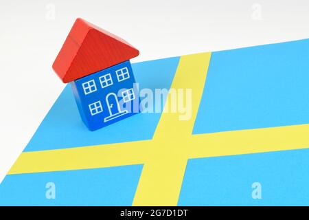 Ein Spielzeughaus, das auf einer schwedischen Flagge sitzt. Ein Stillleben auf dem schwedischen Immobilienmarkt. Stockfoto