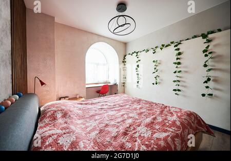 Seitenansicht der modernen Möbel mit großem Bett in bunten Farben, trendigen Lampen und hellem Licht vom Fenster. Konzept der modernen Innenausstattung im Schlafzimmer. Stockfoto