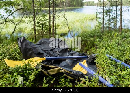 Neu, noch nicht aufgeblasen, Gummiboot und Ruder liegen im Gras, im Wald, am Ufer des Sees. Vorbereitung für den Fischfang. Stockfoto