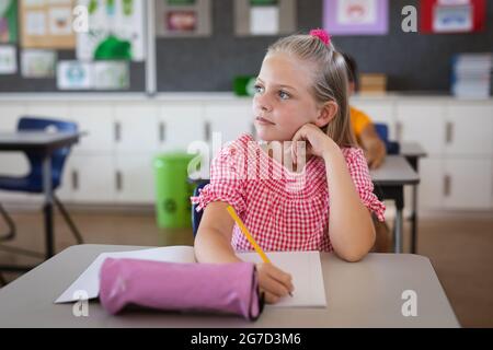 Kaukasisches Mädchen, das in der Schule auf ihrem Schreibtisch sitzt Stockfoto