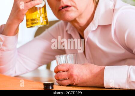 Alte Frau mit Alkohol Problem zu Hause trinken Schnaps sitzen Stockfoto