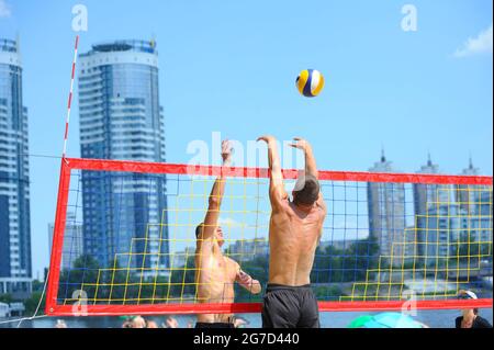 Beachvolleyball. Männlicher Volley-Spieler schlägt über das Netz angreifend, ein anderer blockiert den Ball. Stockfoto