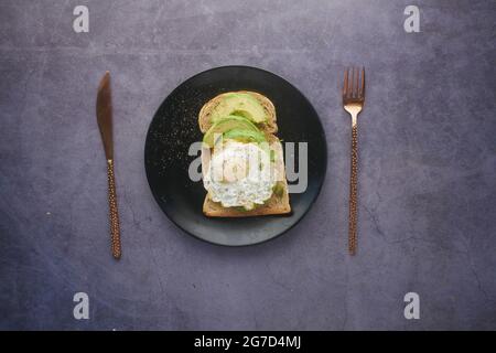 Avocado, braunes Brot, Ei und Rosmarin auf schwarzem Hintergrund Stockfoto