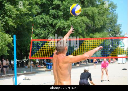 Beachvolleyball. Männlicher Volleyballspieler, der den Ball vor dem Netz serviert, Rückansicht, unscharfe Spieler. Stockfoto