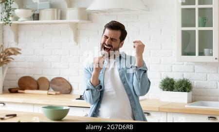 Guy hält Quirl öffnet Mund singen Lied stehen in der Küche Stockfoto