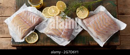Draufsicht Komposition aus ungekochten Meerespollack-Fischfilet auf Papier auf Holztisch mit saftigen Zitronenscheiben Stockfoto